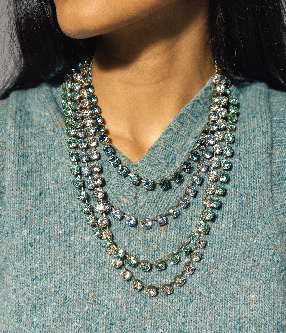 Close-up of a person wearing a multi-layered necklace on a teal sweater.